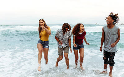 Fröhliche junge Freunde, die aus dem Meerwasser steigen, multiethnische Männer und Frauen, die am Strand spazieren gehen. - JLPSF21543