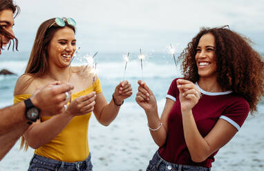 Multi-ethnic group of young people with sparklers at the beach. Group of men and women having fun with sparklers outdoors at the beach. - JLPSF21551