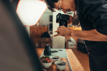 Männlicher Fotograf, der Essen auf dem Tisch fotografiert. Professioneller Food-Fotograf, der Essen für eine Werbung fotografiert. Männlicher Fotograf, der Essen fotografiert - JLPSF21553