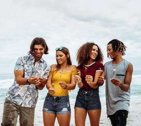 Group of multi-ethnic friends enjoying at beach with sparklers. Young men and women having fun with fireworks at the sea shore. - JLPSF21557