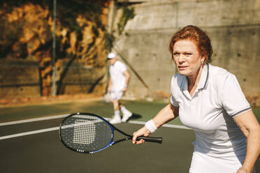 Nahaufnahme einer älteren Frau, die an einem sonnigen Tag Tennis spielt. Ältere Frau auf dem Tennisplatz, die einen Tennisschläger hält und sich auf das Spiel konzentriert. - JLPSF21569