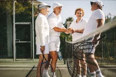 Ältere Männer schütteln sich nach dem Spiel am Netz stehend die Hände. Glückliche Senioren begrüßen sich nach einem Spiel des gemischten Doppel-Tennis. - JLPSF21570