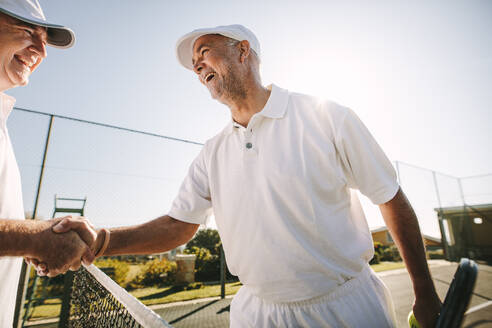 Zwei fröhliche ältere Tennisspieler schütteln sich auf dem Tennisplatz die Hände. Glückliche Tennisspieler begrüßen sich nach einem Tennisspiel. - JLPSF21580