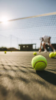 Mann spielt Tennis an einem sonnigen Tag mit Tennisbällen auf dem Platz. Nahaufnahme eines Tennisballs, der auf dem Boden liegt. - JLPSF21583