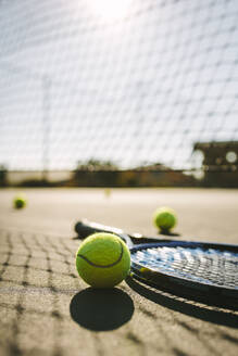 Ebenerdige Aufnahme eines Tennisschlägers mit Bällen auf einem Tennisplatz. Tennisschläger und Bälle liegen neben einem Netz auf einem Tennisplatz an einem sonnigen Tag. - JLPSF21584