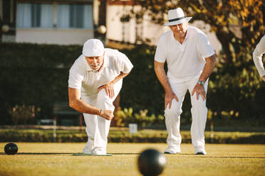 Zwei ältere Männer spielen Boule in einem Park. Ältere Männer genießen ein Boule-Spiel auf einer Wiese an einem sonnigen Tag. - JLPSF21586