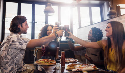 Eine Gruppe gemischtrassiger Freunde stößt in einem Restaurant mit Cola-Gläsern an. Junge Leute sitzen an einem Tisch und genießen eine gemeinsame Mahlzeit. - JLPSF21594