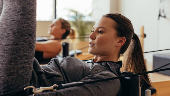 Frau macht Pilates-Training auf einem Fitnessgerät. Fitness-Frauen machen Dehnungsübungen mit Pilates-Stretching-Geräten. - JLPSF21596