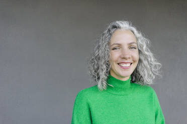 Happy woman with gray curly hair in front of wall - SEAF01446