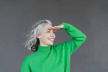 Happy woman with gray hair shielding eyes in front of wall - SEAF01460