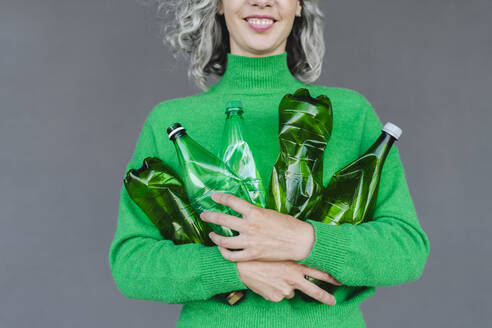 Lächelnde Frau mit Plastikflaschen vor einer Wand - SEAF01468