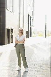 Businesswoman standing with arms crossed on footpath in front of building - SEAF01501