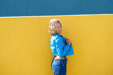 Lächelnde Frau in blauer Lederjacke vor einer Wand - OIPF02591