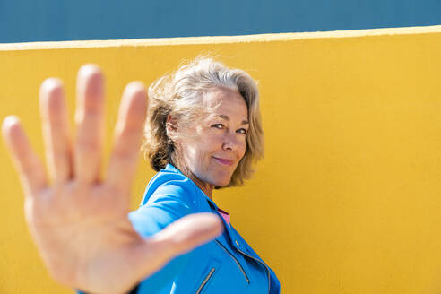 Smiling woman doing stop gesture by colored wall - OIPF02594