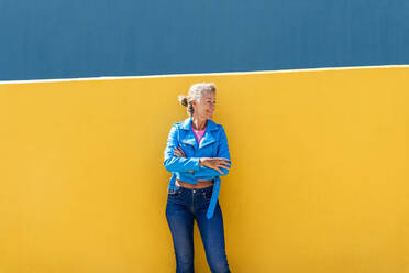 Mature woman with arms crossed leaning on colored wall - OIPF02597