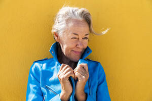 Glückliche reife Frau, die vor einer gelben Wand zwinkert - OIPF02603