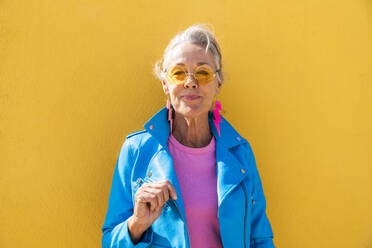 Smiling mature woman wearing sunglasses in front of yellow wall - OIPF02604