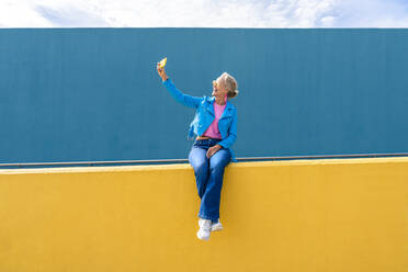 Glückliche reife Frau nimmt Selfie durch Handy auf Wand - OIPF02628