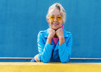 Smiling mature woman with hands on chin in front of blue wall - OIPF02638