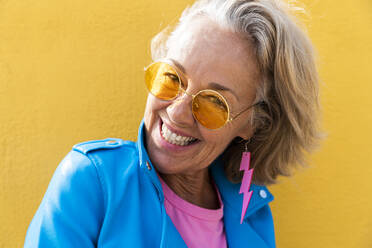Happy mature woman wearing sunglasses in front of yellow wall - OIPF02640