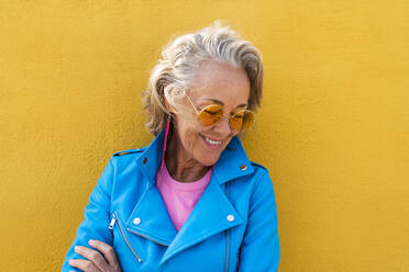 Smiling woman wearing sunglasses in front of yellow wall - OIPF02641