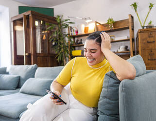 Glückliche junge Frau mit Mobiltelefon auf dem Sofa - AMRF00111