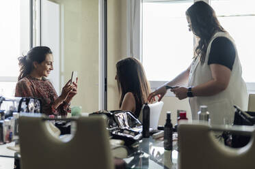 Lächelnde Visagistin, die eine Kundin mit dem Smartphone fotografiert, und Friseur, der die Haare zurechtrückt - PGF01314