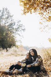 Girl sitting with sister in autumn forest - YLF00018
