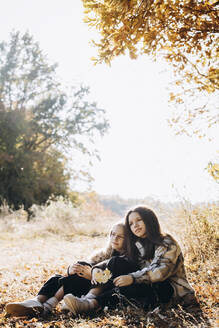 Mädchen sitzt mit Schwester im Herbstwald - YLF00018