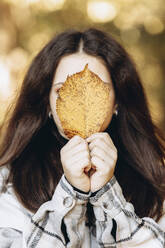 Girl covering face with yellow leaf - YLF00021