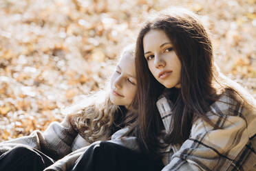 Mädchen mit Schwester sitzt im Wald an einem sonnigen Tag - YLF00023