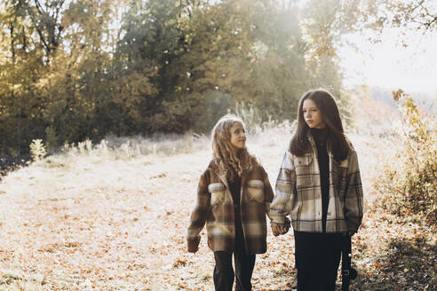 Mädchen hält Hände mit Schwester und Spaziergang im Wald an einem sonnigen Tag - YLF00024