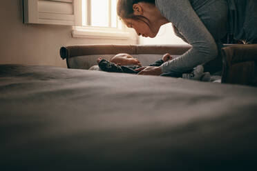 Mother putting her baby to sleep in his crib. Woman bending forward to lay the baby on the bed. - JLPSF21657