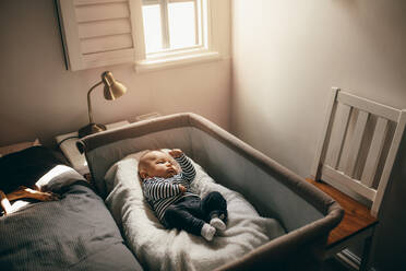 Baby schläft in einem Stubenwagen im Schlafzimmer. Kleinkind liegt auf einem Kinderbett und bewegt seine Hände und Beine. - JLPSF21662