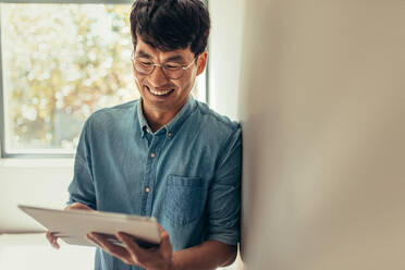 Man using tablet pc and smiling indoors. Man at home reading something funny on digital tablet. - JLPSF21665