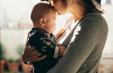 Seitenansicht einer Frau, die ihr Baby trägt und ihm den Kopf küsst. Ausschnitt einer jungen Mutter, die ihr Baby verwöhnt. - JLPSF21670