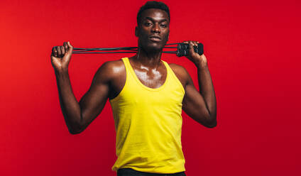 Muskulöser Mann posiert mit Springseil auf rotem Hintergrund. Afrikanisches Fitnessmodell mit Springseil. - JLPSF21673