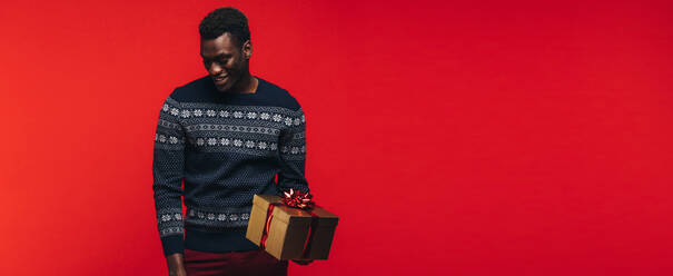 Young african guy holding a gift box. African american man with a present on red background. - JLPSF21707