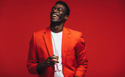 Handsome young african man with a glass of champagne. Smiling young guy having champagne against red background. - JLPSF21727