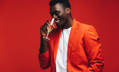 Stylish young man in red jacket drinking champagne. African american man having a glass of champagne against red background. - JLPSF21729