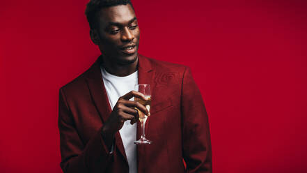 Stylish african man with a glass of champagne looking away at copy space. Man in red jacket having champagne against colored background. - JLPSF21730