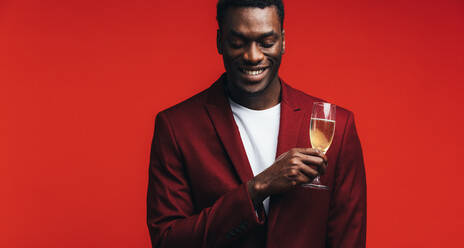 Relaxed young man with a glass of champagne and thinking against colored background. Man remembering a special moment while having a glass of champagne. - JLPSF21731