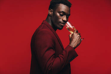 Good looking african guy drinking champagne against red background. Sophisticated african man having a glass if champagne. - JLPSF21734