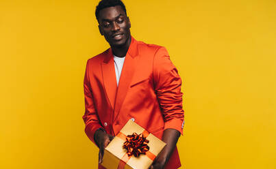 Stilvoller afrikanischer Mann mit einer Geschenkbox. Modischer junger Mann mit einem Geschenk vor gelbem Hintergrund. - JLPSF21741