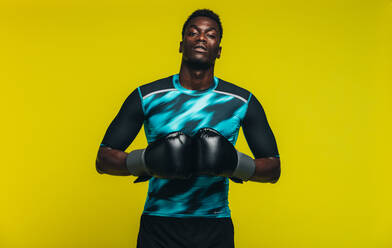 African man in sportswear with boxing gloves looking at camera against yellow background. Fit young male boxer. - JLPSF21746
