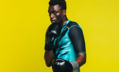 Afrikanischer Mann in Boxstellung vor gelbem Hintergrund. Mann in Sportkleidung mit Boxhandschuhen übt seine Bewegungen. - JLPSF21747