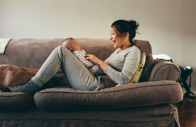 Frau auf einer Couch liegend, die ihr Baby verwöhnt. Lächelnde Mutter, die mit ihrem Kleinkind spricht und spielt. - JLPSF21783