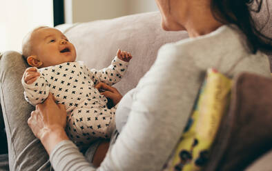 Ausschnitt einer Frau, die auf der Couch sitzt und ihr Kleinkind hält. Rückansicht einer Mutter, die mit ihrem Baby spielt. - JLPSF21784