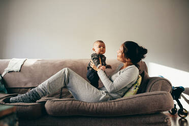 Junge Mutter spricht mit ihrem Baby, während sie sich auf einer Couch entspannt. Frau hält ihr Kleinkind und spricht mit ihm. - JLPSF21789