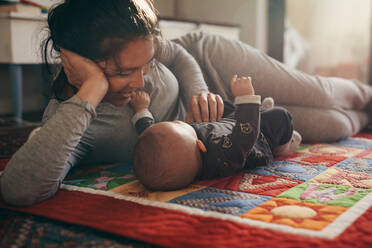 Lächelnde Mutter spielt mit ihrem Baby auf dem Bett liegend. Frau verwöhnt und spricht mit ihrem Baby. - JLPSF21791